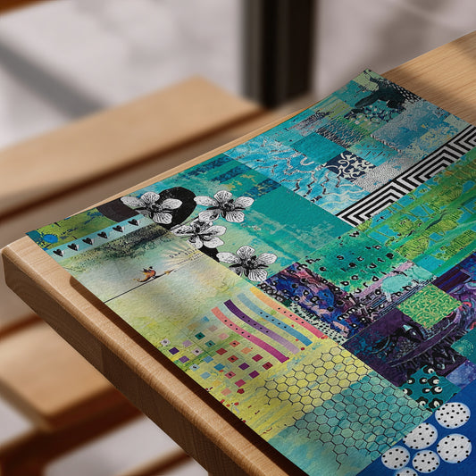 A colorful patchwork-style art print featuring abstract floral and geometric designs in teal, green, blue, yellow, purple, black, and white, displayed on a wooden frame in a softly blurred indoor setting.