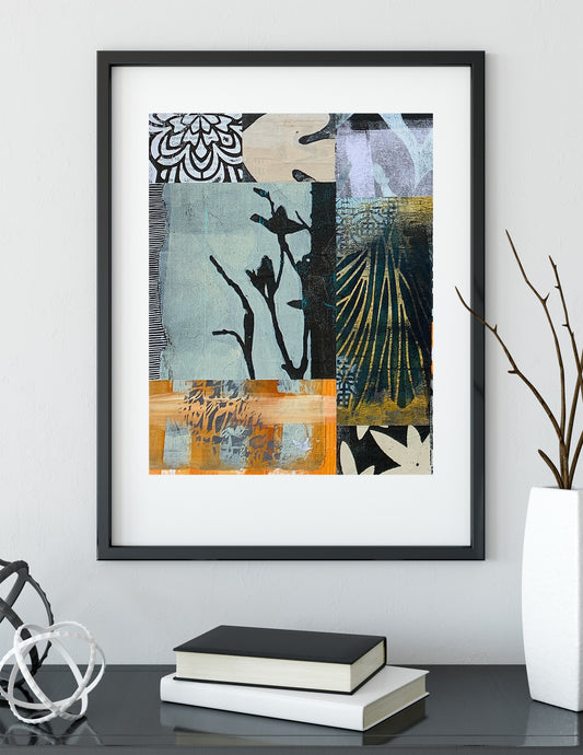 A framed abstract art print with a black frame and white mat, hanging on a light gray wall above a dark table with books and decorative objects.