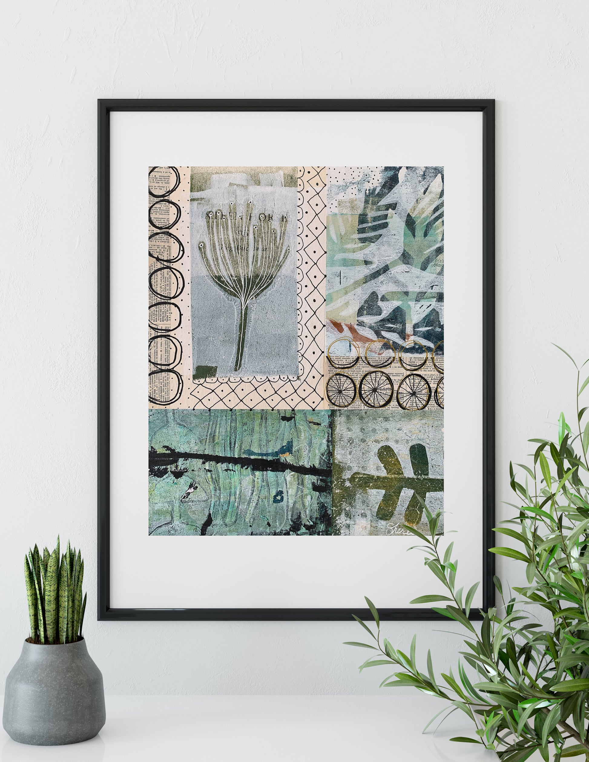 A framed art print featuring a patchwork collage of botanical and abstract designs in muted green, beige, and gray tones, displayed on a white wall above a shelf with a small potted plant and green foliage.