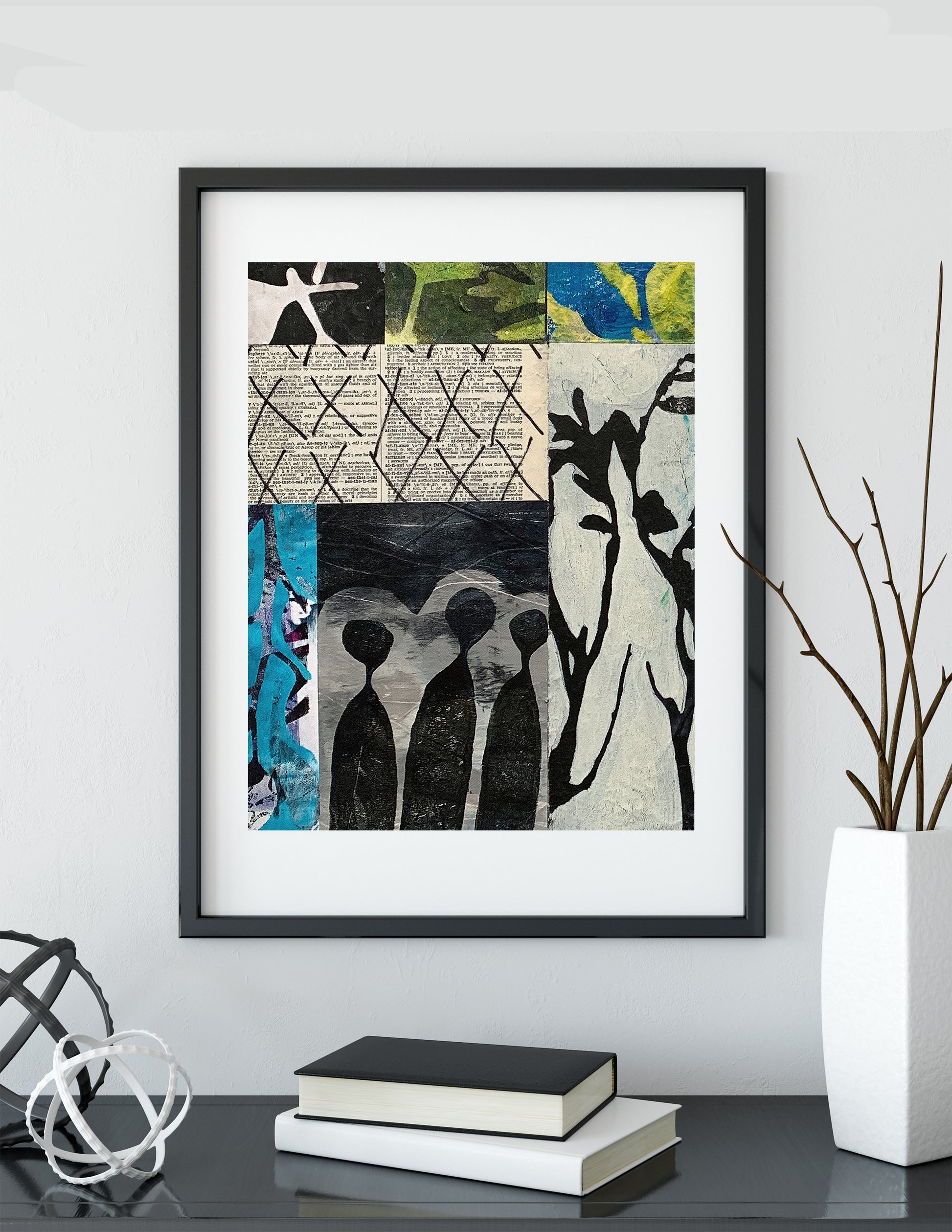 Framed abstract art print featuring black silhouettes and textured collage panels in black, white, beige, blue, green, and yellow, displayed on a shelf in a modern interior setting.