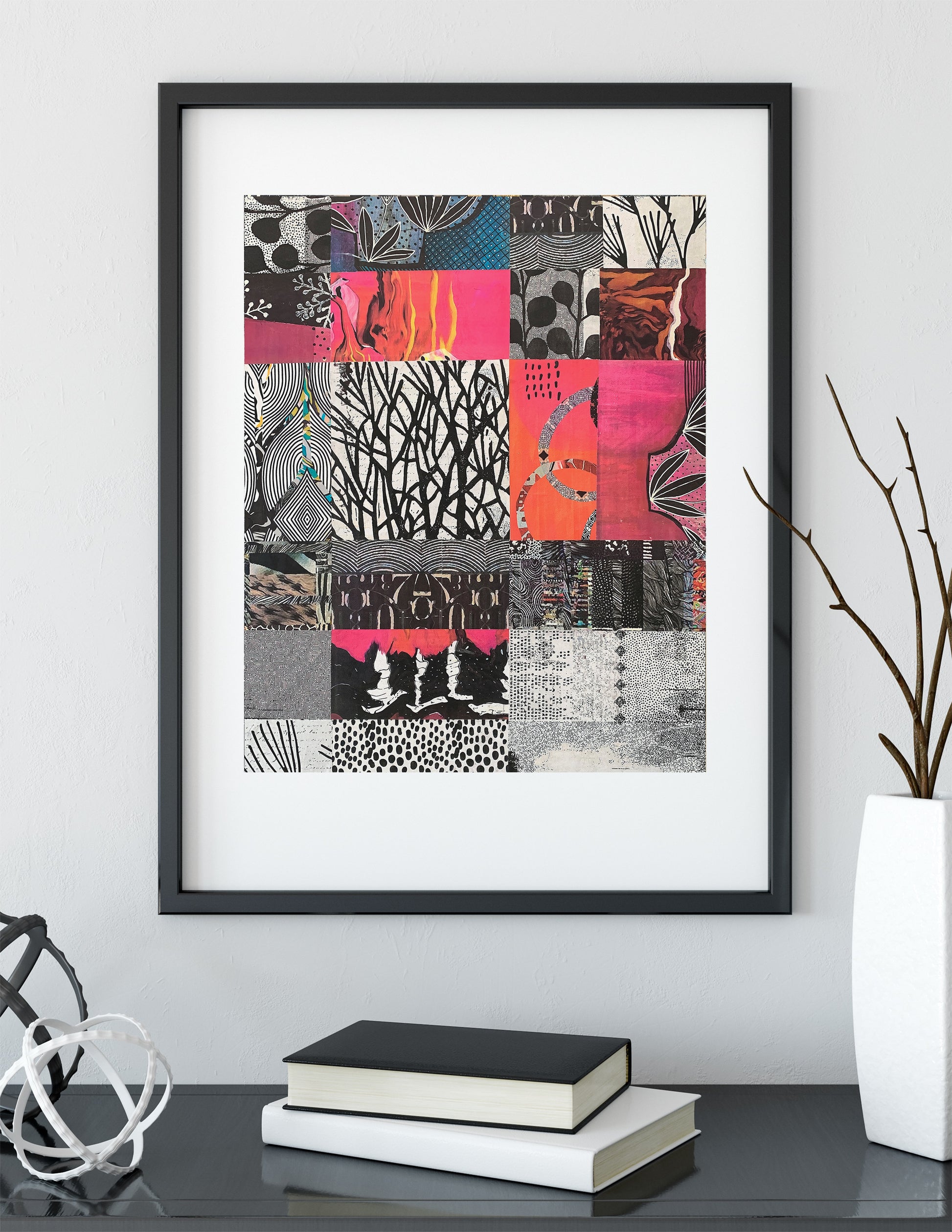 A framed abstract art print featuring a colorful patchwork of black, pink, orange, and gray patterns, displayed on a shelf with books and a vase in a modern room setting.