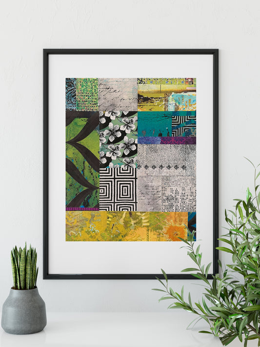 A framed abstract patchwork art print with a black frame and white mat, featuring a colorful collage of patterns and textures in green, yellow, blue, black, and white. The framed print is displayed on a white surface next to a small potted succulent and a green leafy plant.