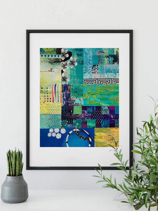 A framed abstract art print featuring a vibrant patchwork design in shades of teal, blue, green, yellow, and purple, styled on a white surface with a small potted succulent on the left and a green plant on the right.