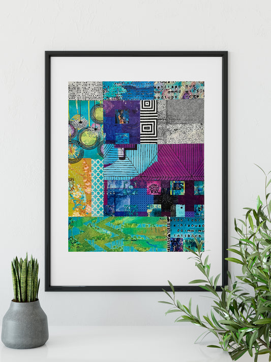 A framed abstract art print featuring a vibrant patchwork design with blues, purples, greens, and grays, styled on a white surface with a small potted succulent and a green plant in the foreground.