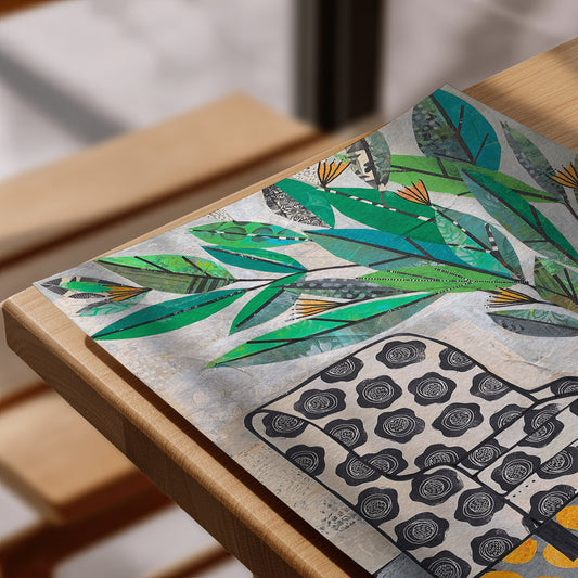 A close-up of a decorative art print featuring green tropical leaves and black-and-white floral motifs, styled on a light wood frame.