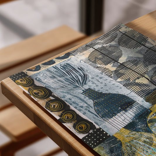 A close-up of a rectangular art print  with an abstract, artistic pattern featuring blue, black, yellow, and beige tones, resting on a light wood frame.