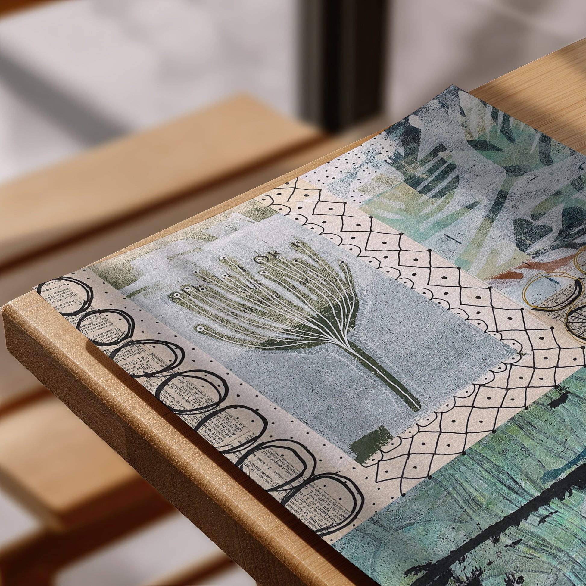 A close-up of a rectangular art print with a mixed-media collage design featuring botanical motifs, geometric patterns, and vintage-style text elements, styled on a light wood frame.