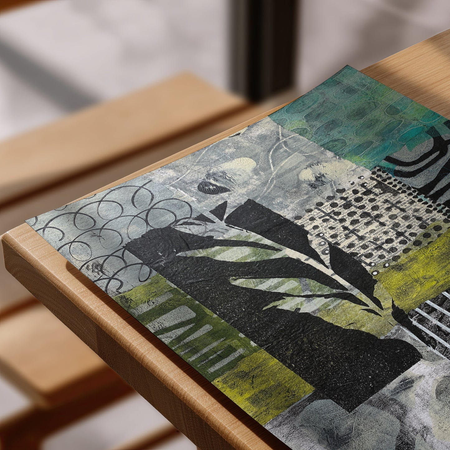 An abstract mixed-media art print featuring black, gray, teal, and olive green patterns, displayed on a light wood rame.