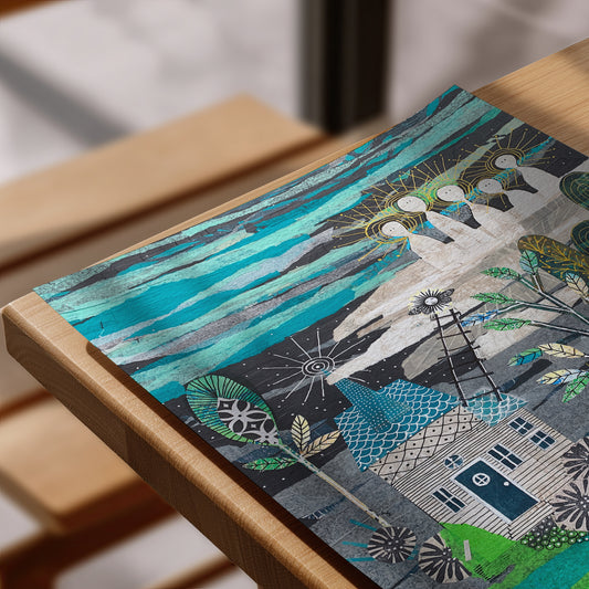 A close-up of a colorful art print featuring a whimsical house, trees, and abstract sky, resting on a light wood table.