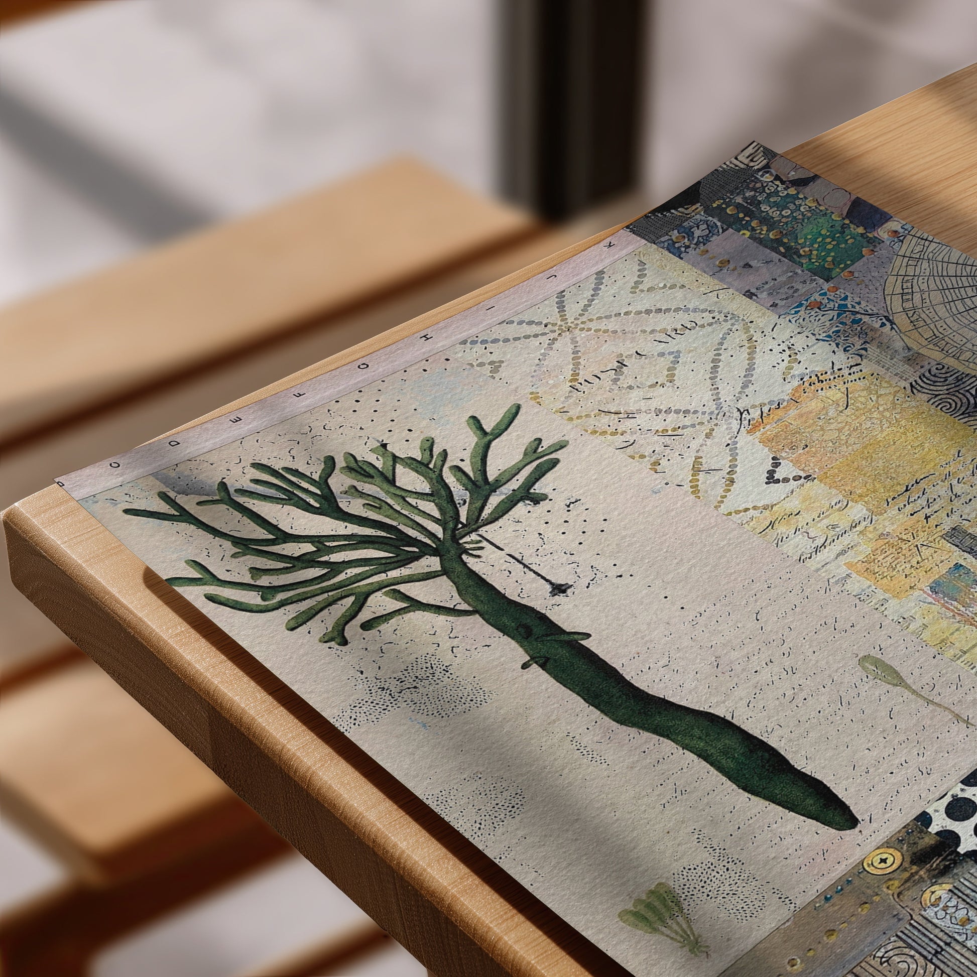 A close-up of a printed art piece or poster laid on a wooden table, featuring a green coral-like tree illustration over a textured beige background with mixed abstract and nautical-style patterns.