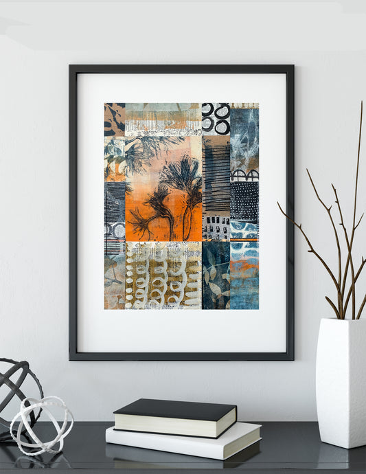 Framed abstract art print with a black frame and white mat, featuring a patchwork design in orange, blue, beige, and black, displayed on a shelf next to books and a vase.