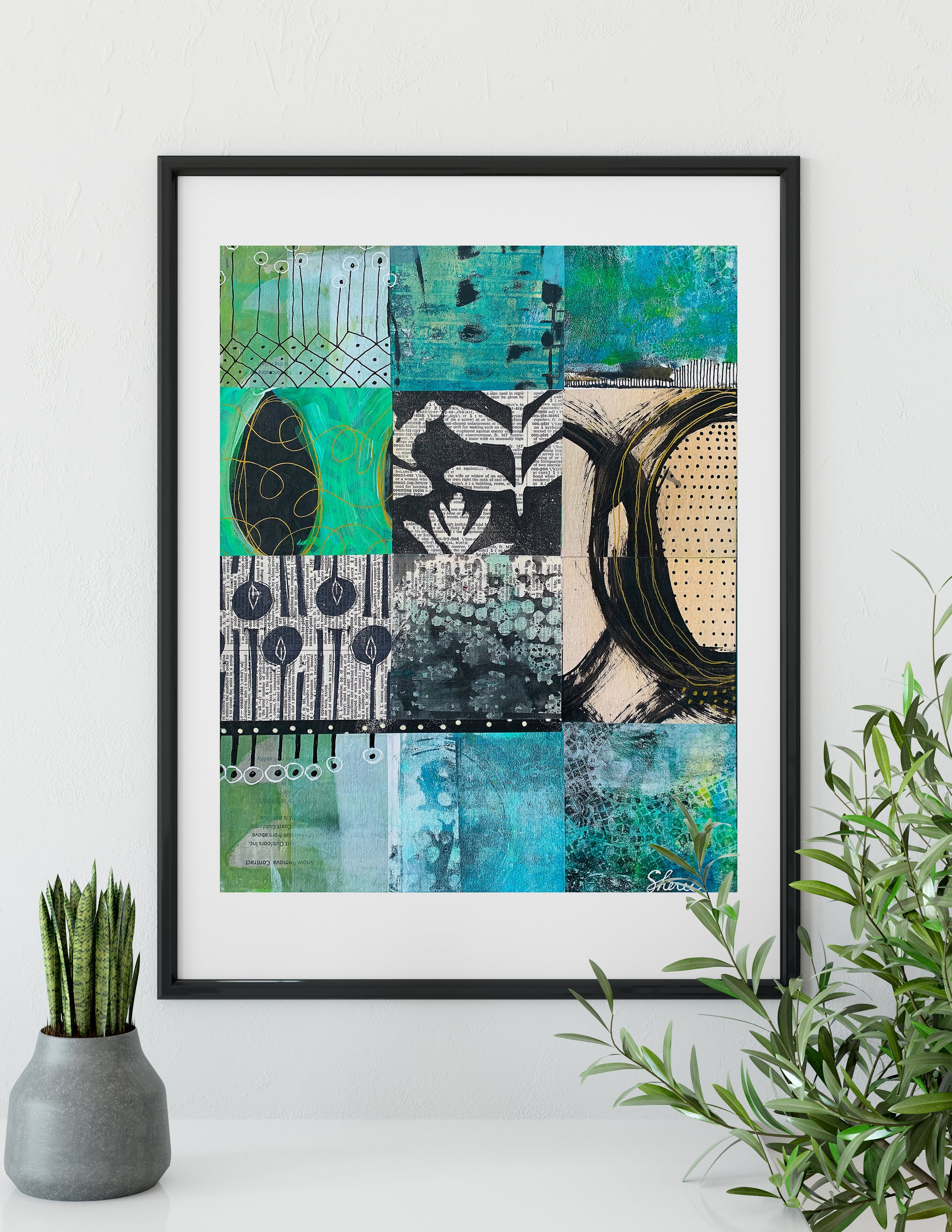 A framed abstract art print featuring a patchwork of teal, green, black, and beige textured designs, displayed on a white wall above a shelf with a small potted succulent and a green plant.