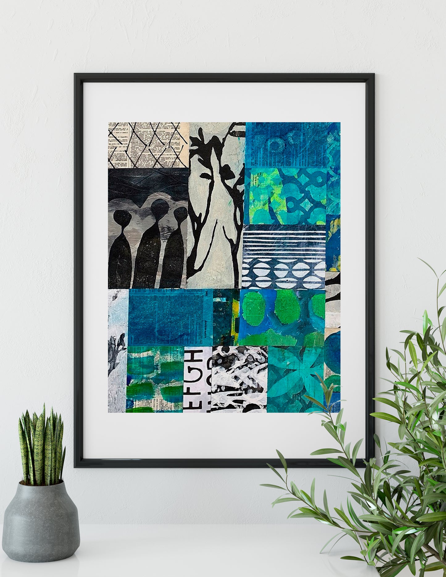 A framed abstract art print featuring a 3x3 grid of blue, green, black, and white patterns, displayed on a white wall above a shelf with a small potted plant and a green leafy branch.