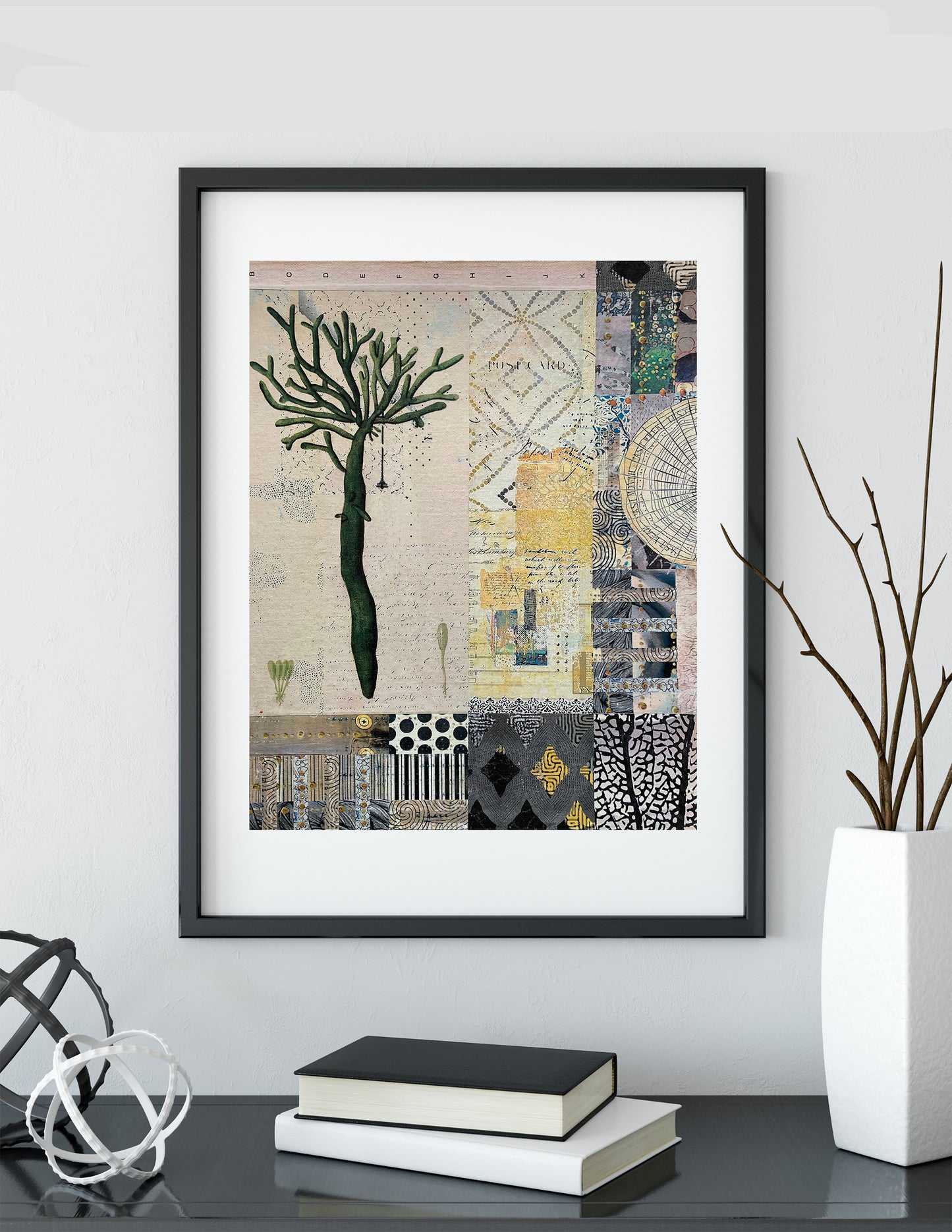 A framed art print featuring a collage of abstract patterns and a stylized tree, displayed on a shelf in a modern room setting with books and a vase.