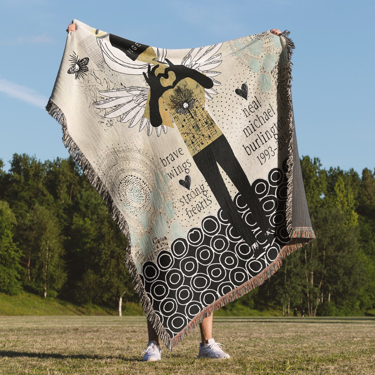 Person holding a decorative blanket with artistic design in an outdoor setting
