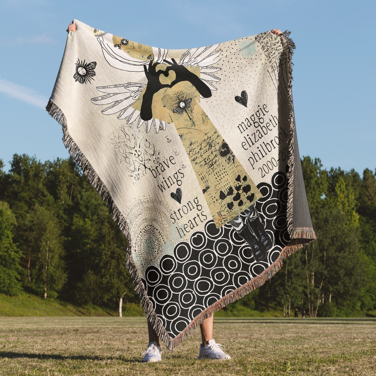 Person holding a decorative blanket with artistic designs and text in an outdoor setting.