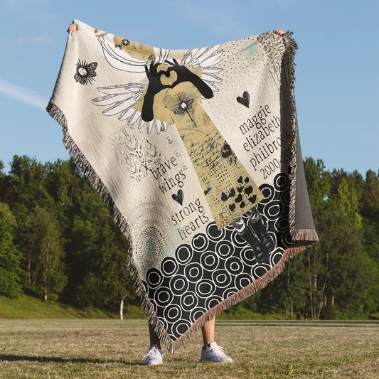 Person holding a decorative blanket with artistic designs and text in an outdoor setting.