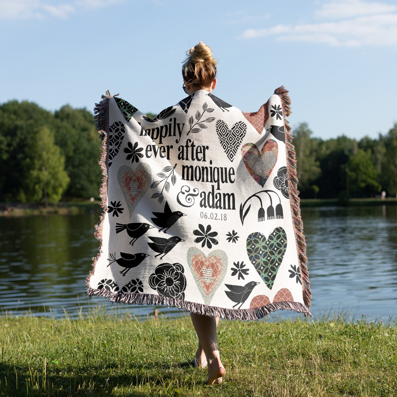 Person holding a personalized blanket with decorative patterns and text by a lake.
