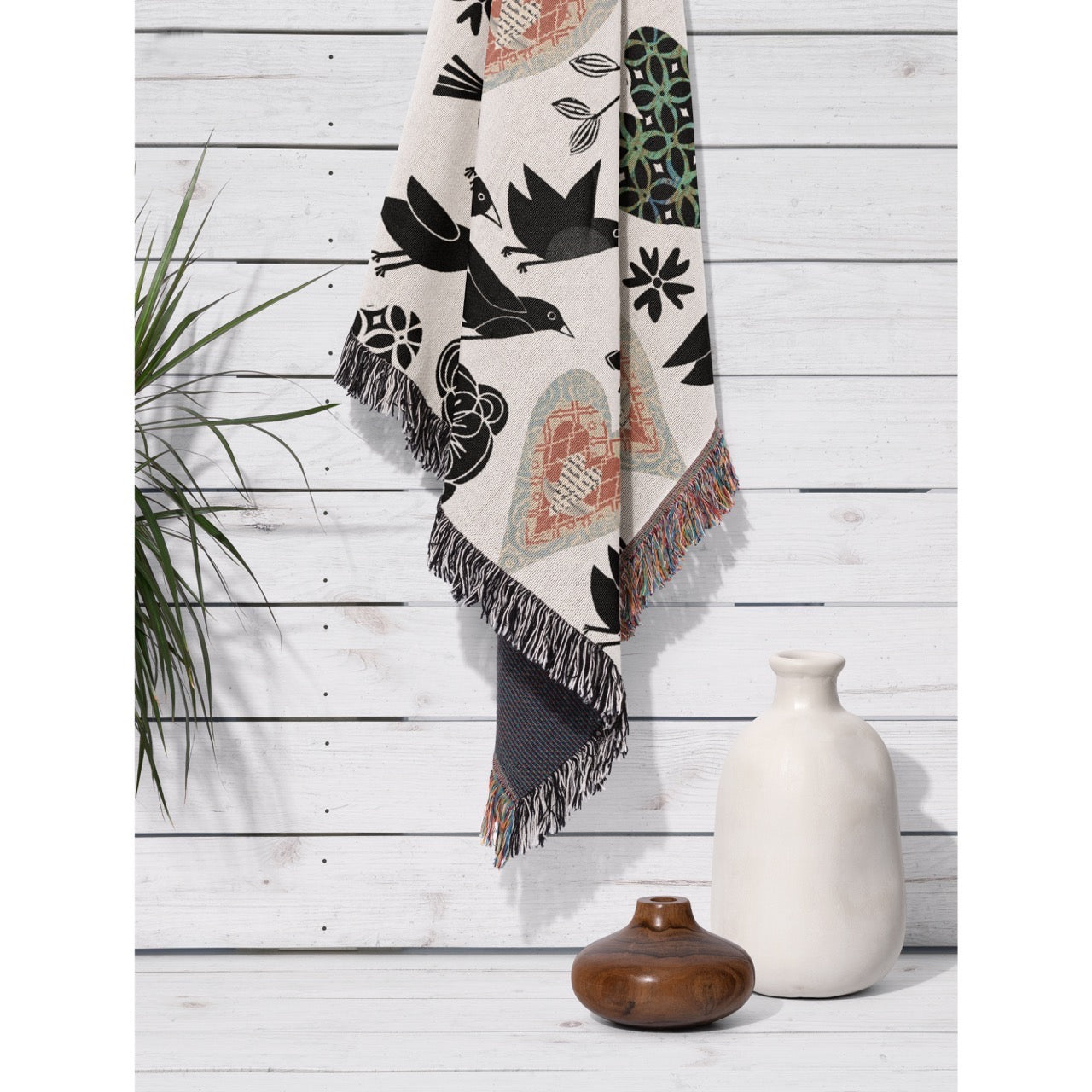 Decorative throw blanket with geometric patterns on a wooden surface with vases and plants.