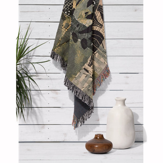 Decorative blanket with fringe hanging on a wooden wall with vases and a plant.