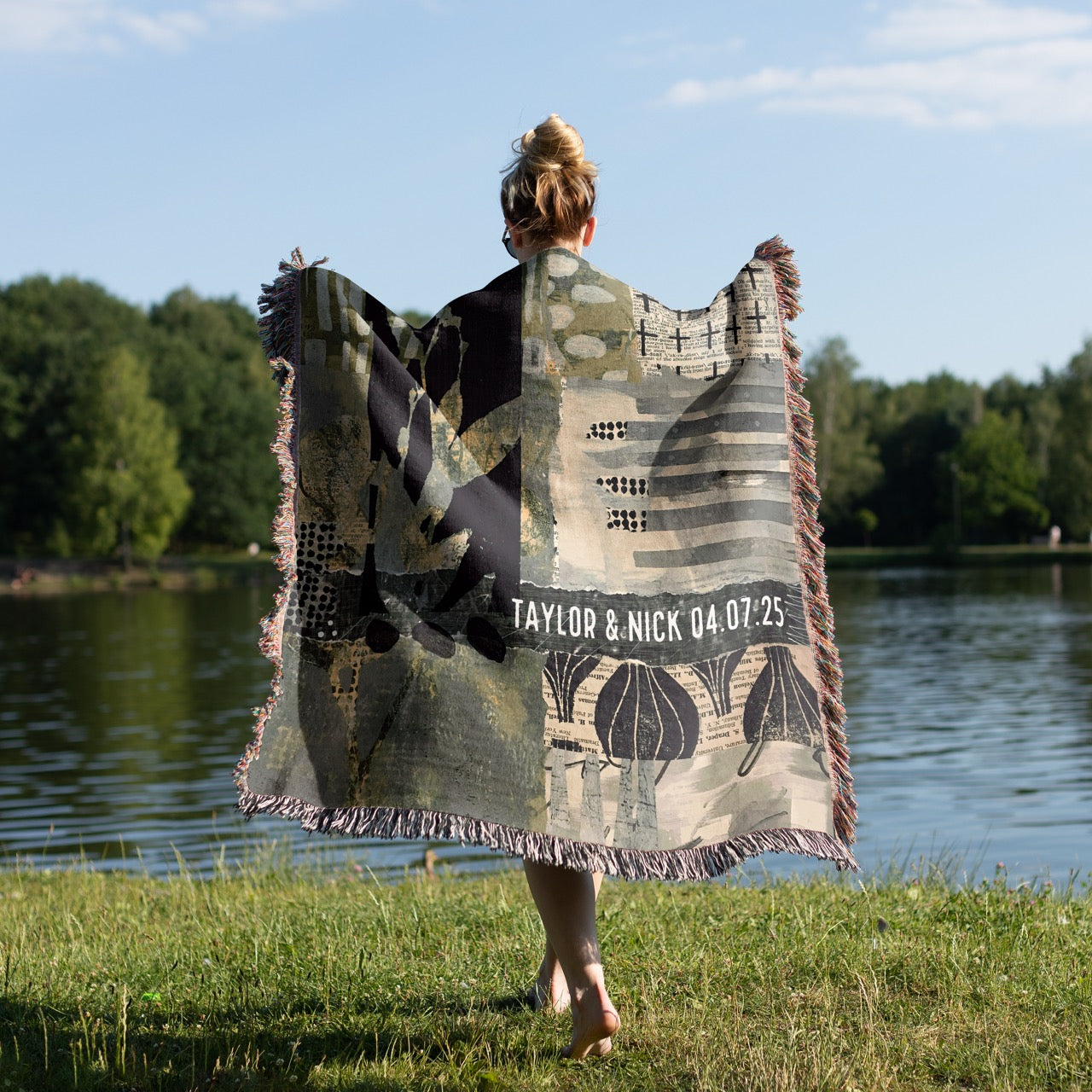Person holding a personalized blanket by a lake with trees in the background