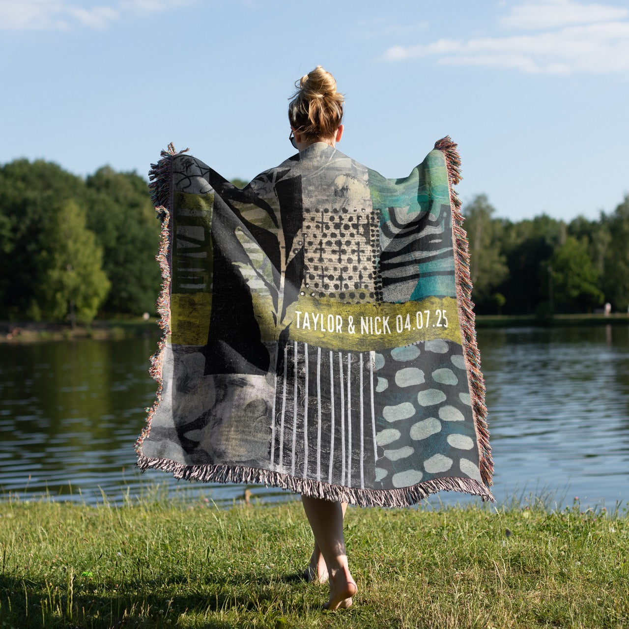 Person holding a personalized blanket by a lake with trees in the background