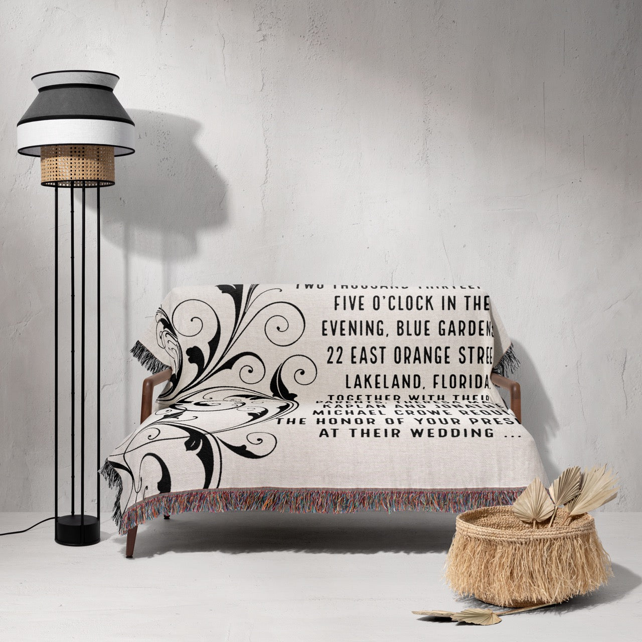 Decorative blanket with text and patterns on a bed against a gray wall with a floor lamp.